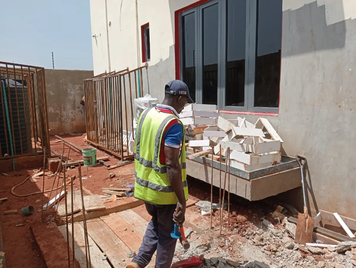 technician wearing a green vest and holding a hammer and another instrument